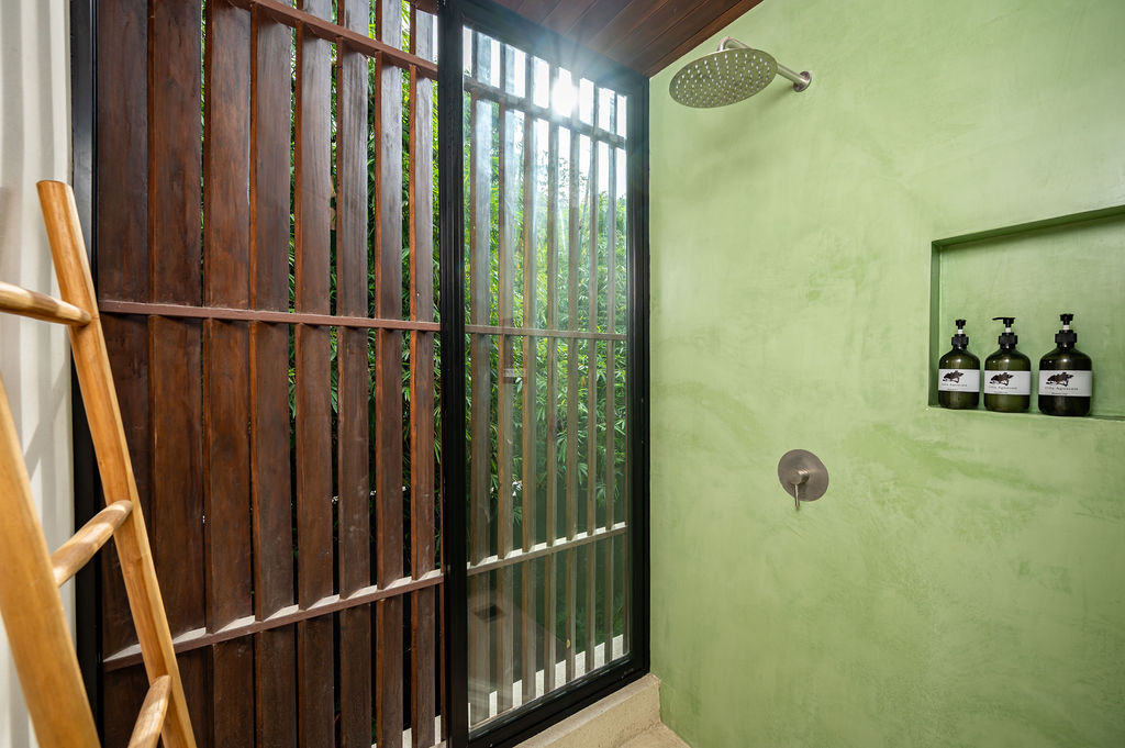 Rain shower against green plaster with a recessed amenity niche, open to a teak slat screen and bamboo