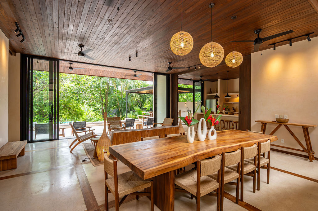 Dining table under woven pendants with the doors open to the pool