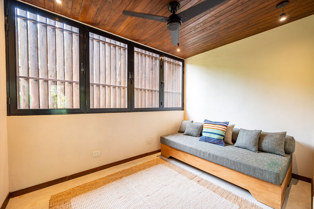 Adjacent daybed room with a built-in teak sofa, grey cushions and timber slat windows